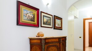 Um corredor com obras de arte emolduradas na parede, um armário de madeira com uma concha decorativa e uma porta que dá para outro quarto.