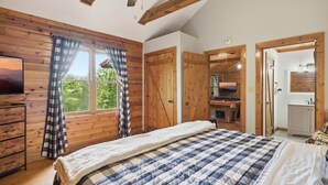 Ein Schlafzimmer mit einem großen Bett, Holzwänden, einem Fernseher und Blick ins Freie.