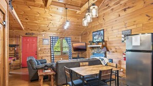 Ein Ferienhaus-Innenraum mit Holzvertäfelung, einer Couch, einem Esstisch, einem Fernseher und einem Kühlschrank.