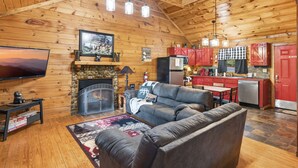 Ein gemütliches Blockhaus-Interieur mit Kamin, Fernseher, einer Couch und einer Küchenzeile.