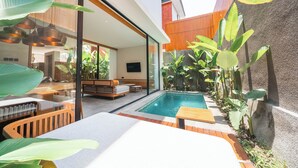 Uma área externa moderna com piscina, assentos e plantas tropicais.