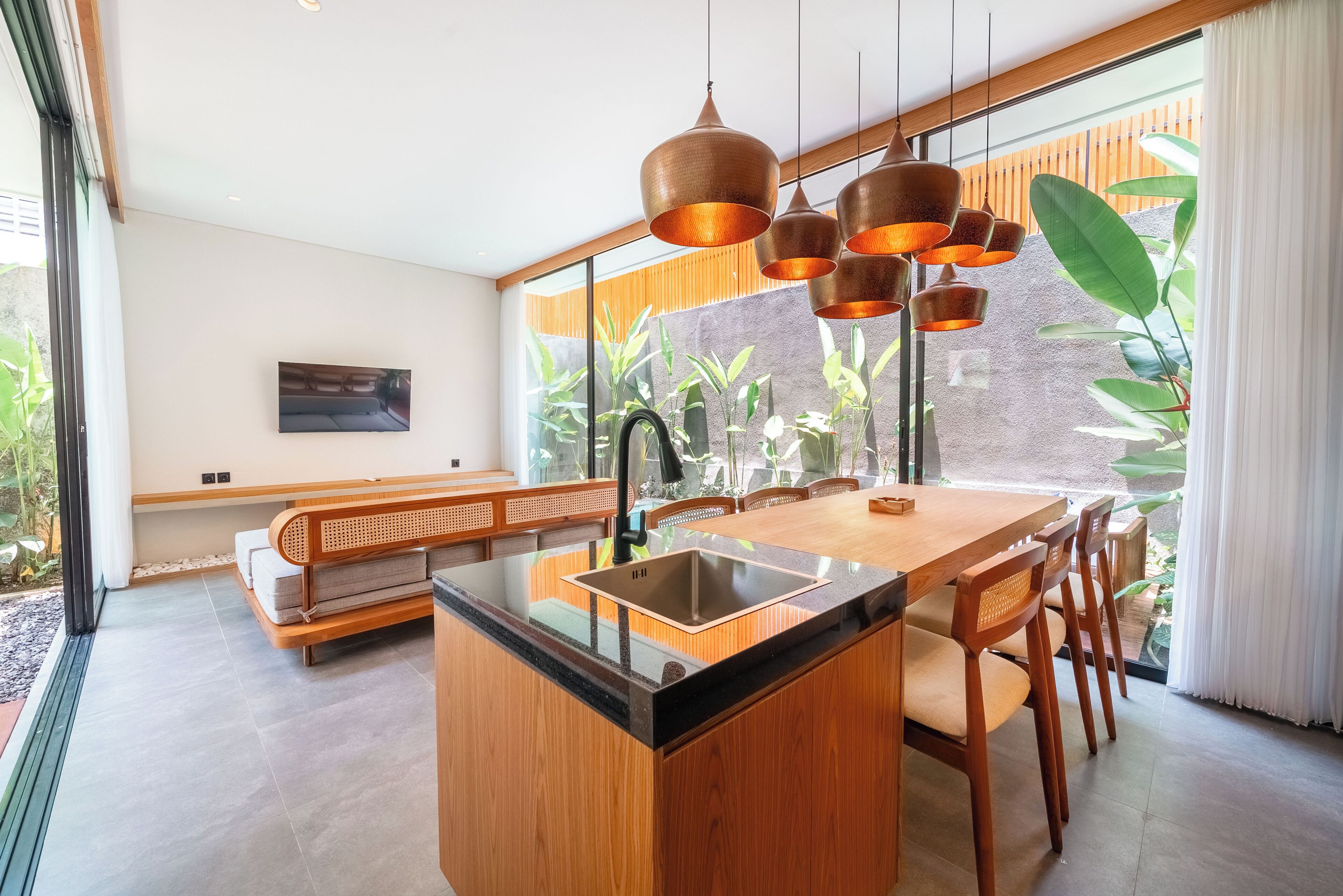 Une cuisine moderne avec un îlot central, des meubles en bois et de grandes fenêtres ornées de plantes.