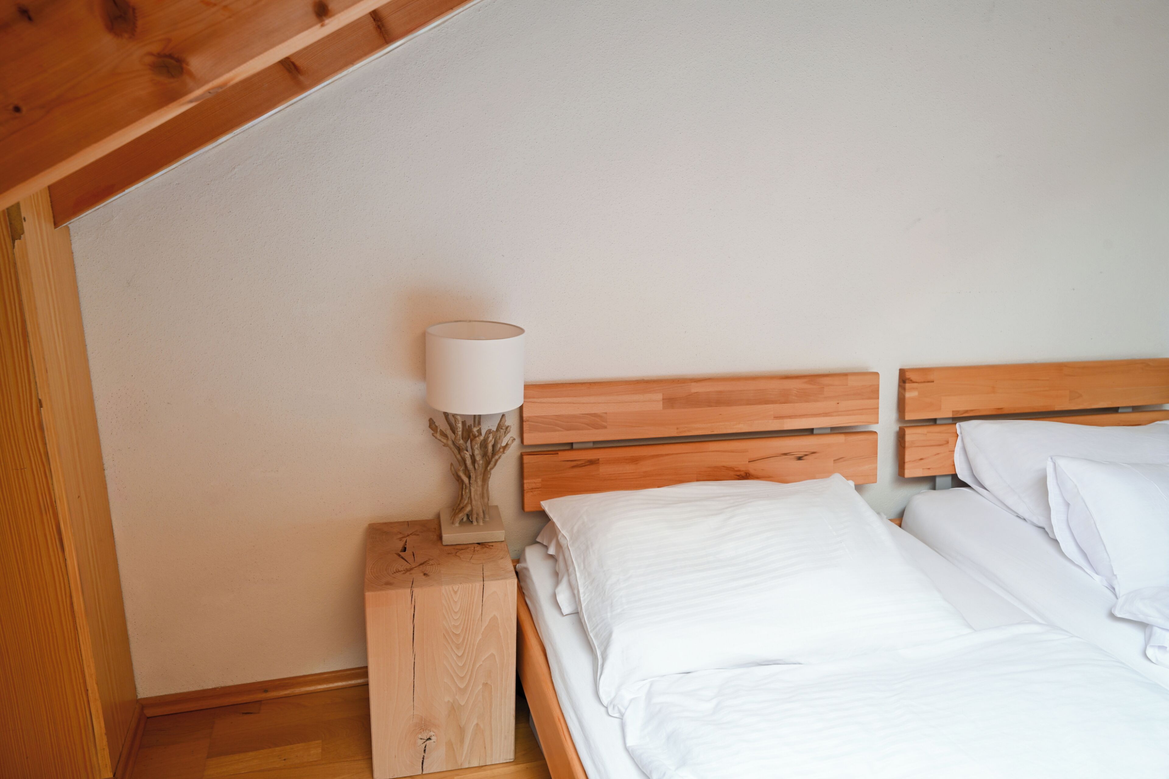 Een slaapkamer met een houten hoofdbord, witte beddengoed en een nachtkastje met een lamp.