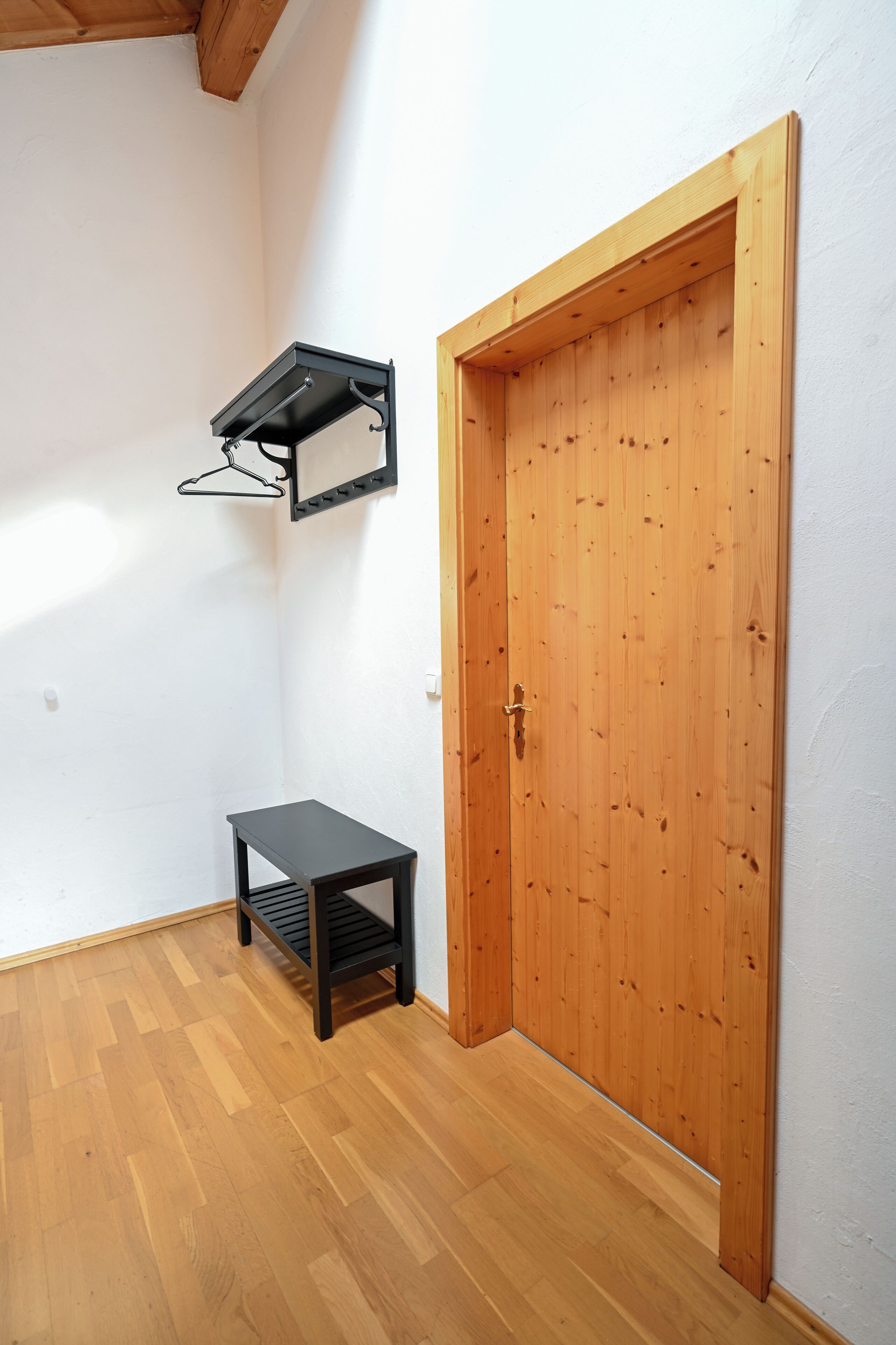 Ein Zimmer mit Holztür, schwarzem Regal und Holzboden.