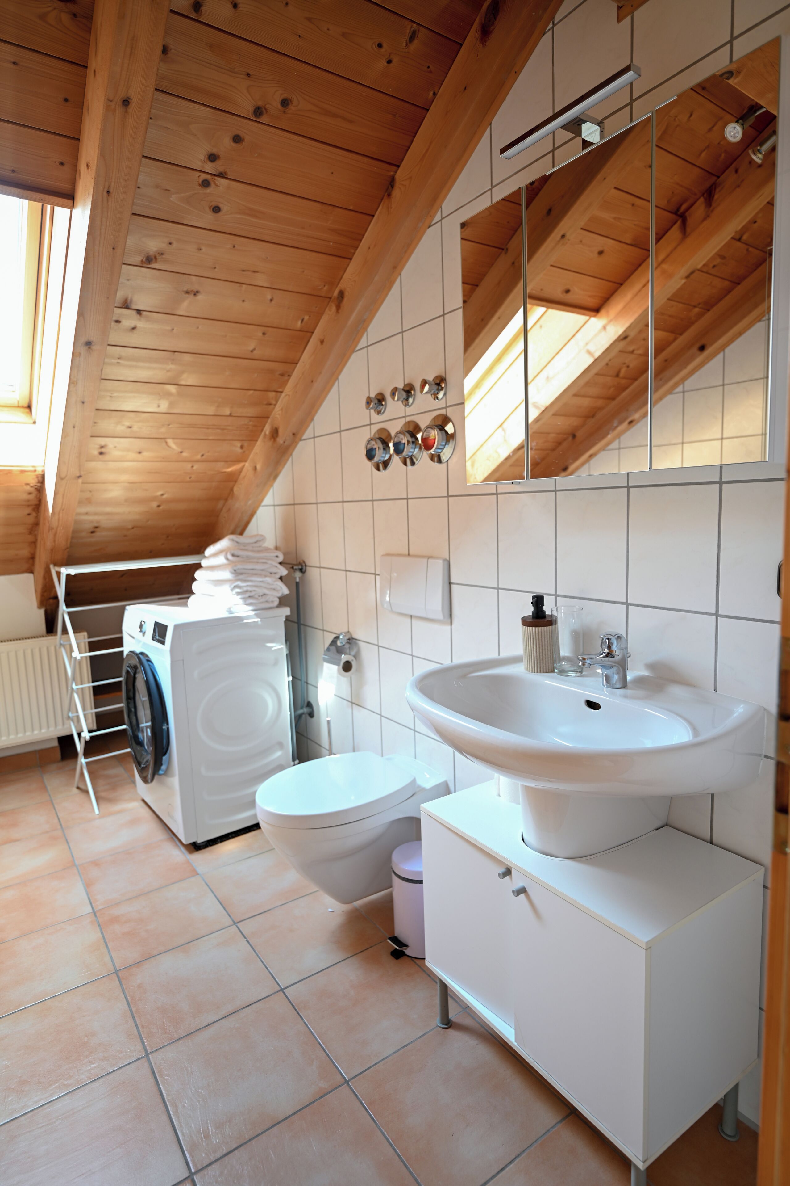 Ein modernes Badezimmer mit Waschmaschine, Toilette, Waschbecken und Spiegel.