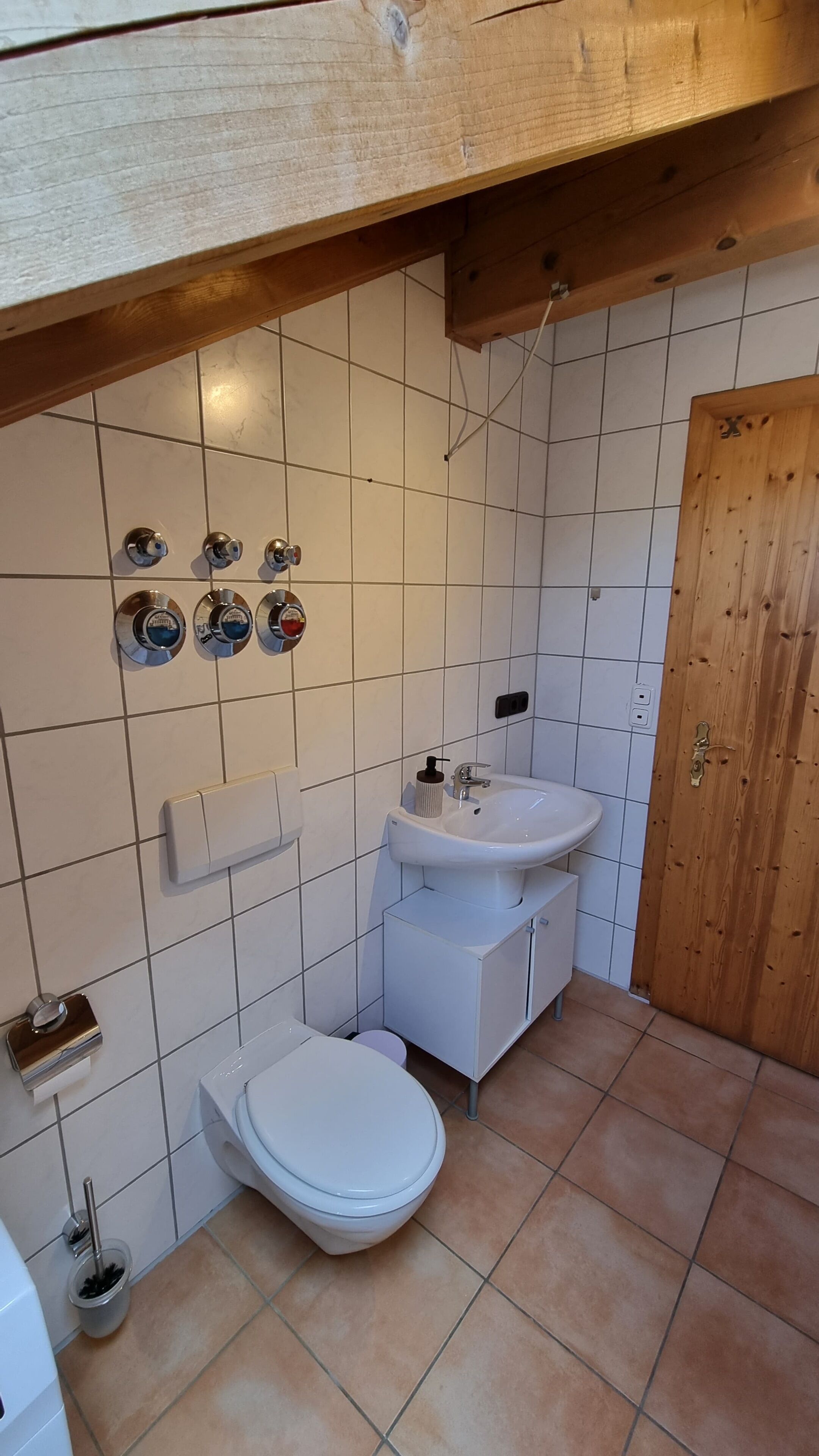 Ett badrum med toalett, handfat och tre väggmonterade blandare.