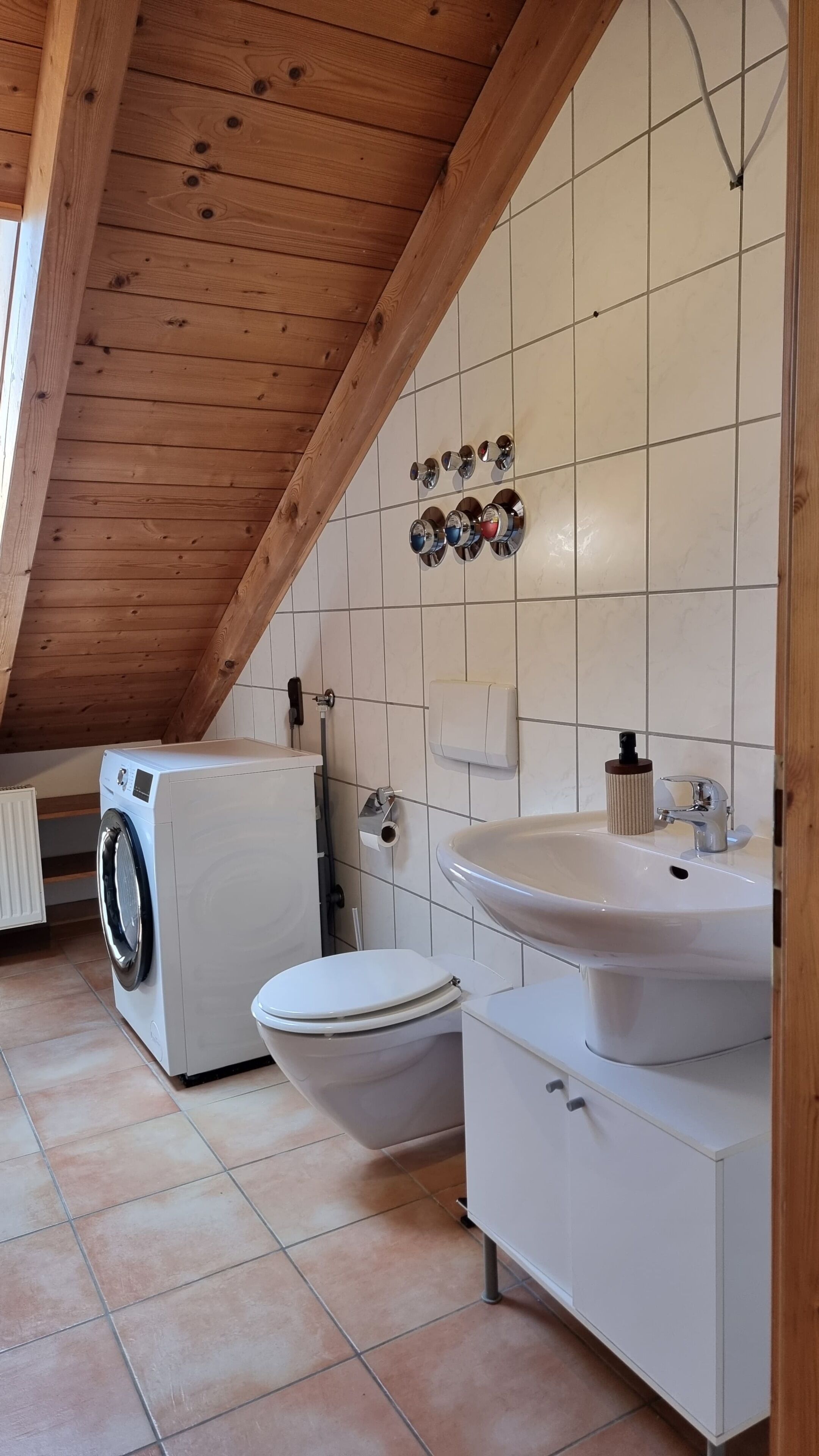 Een kleine badkamer met een wasmachine, toilet, wastafel en betegelde wanden.