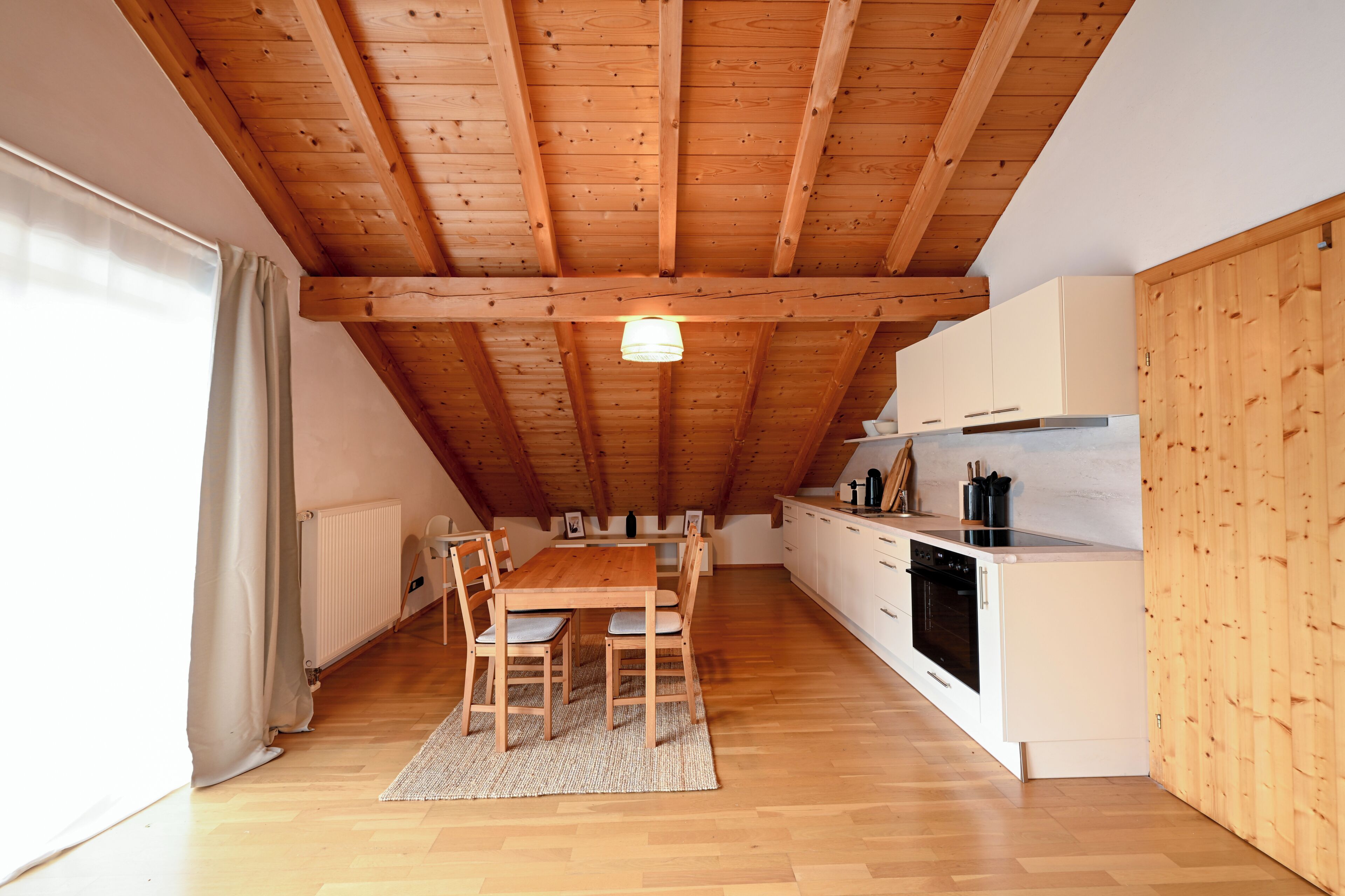 A kitchen with wooden beams, a dining table with chairs, and white cabinets.