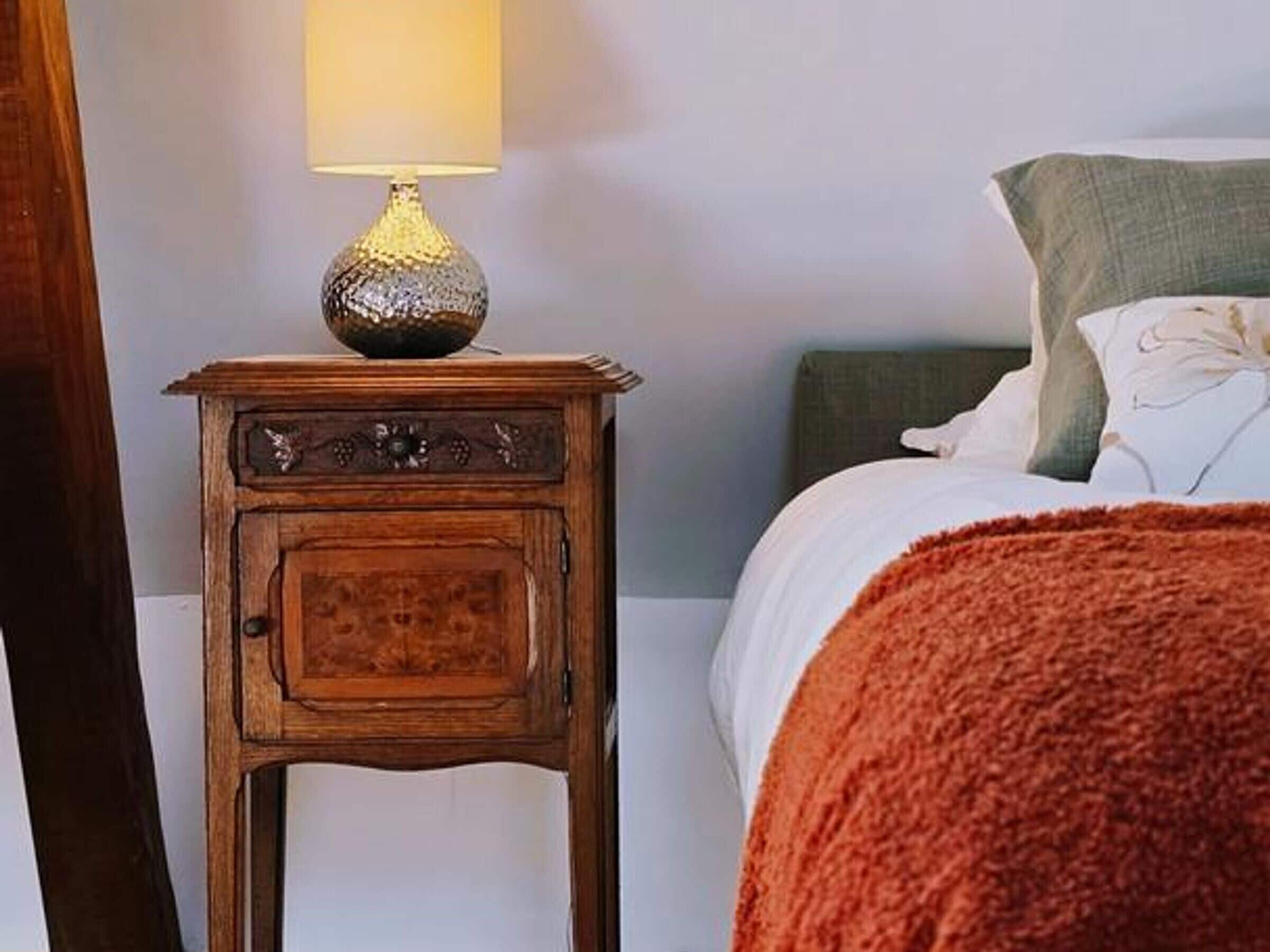 A bed with a green pillow, a wooden nightstand with a lamp, and a red blanket.