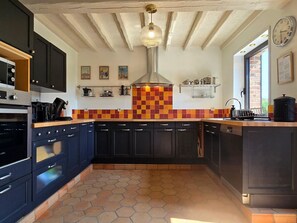 A kitchen with dark cabinets, a tiled backsplash, a hanging light fixture, and a clock on the wall.