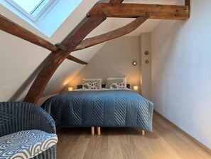 A bedroom with a sloped ceiling, a bed with a blue quilt, two bedside lamps, and a chair.