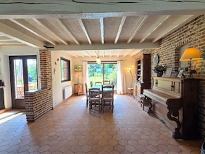 A spacious room with a hexagonal tiled floor, a fireplace, a dining table with chairs, and a piano.