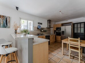 A modern kitchen with a central island, wooden cabinets, a built-in oven, and a dining area with a table and chairs. - Quiet villa, private pool - 6 guests (Biscarrosse)