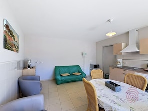 Ein gemütlicher Wohnraum mit einem grünen Sofa, einem Esstisch mit Stühlen, einer Küchenzeile und einem Bild an der Wand.