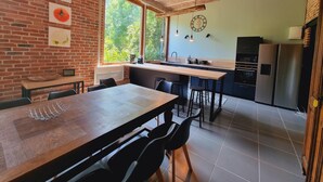 A kitchen with a brick ceiling, a wooden dining table, and a view of greenery outside. - Gîte with pets allowed - 14 guests (Roucourt)