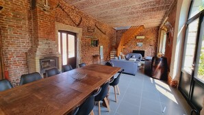 A spacious room with a brick wall, a fireplace, a dining table with chairs, a sofa, and a television. - Gîte with pets allowed - 14 guests (Roucourt)