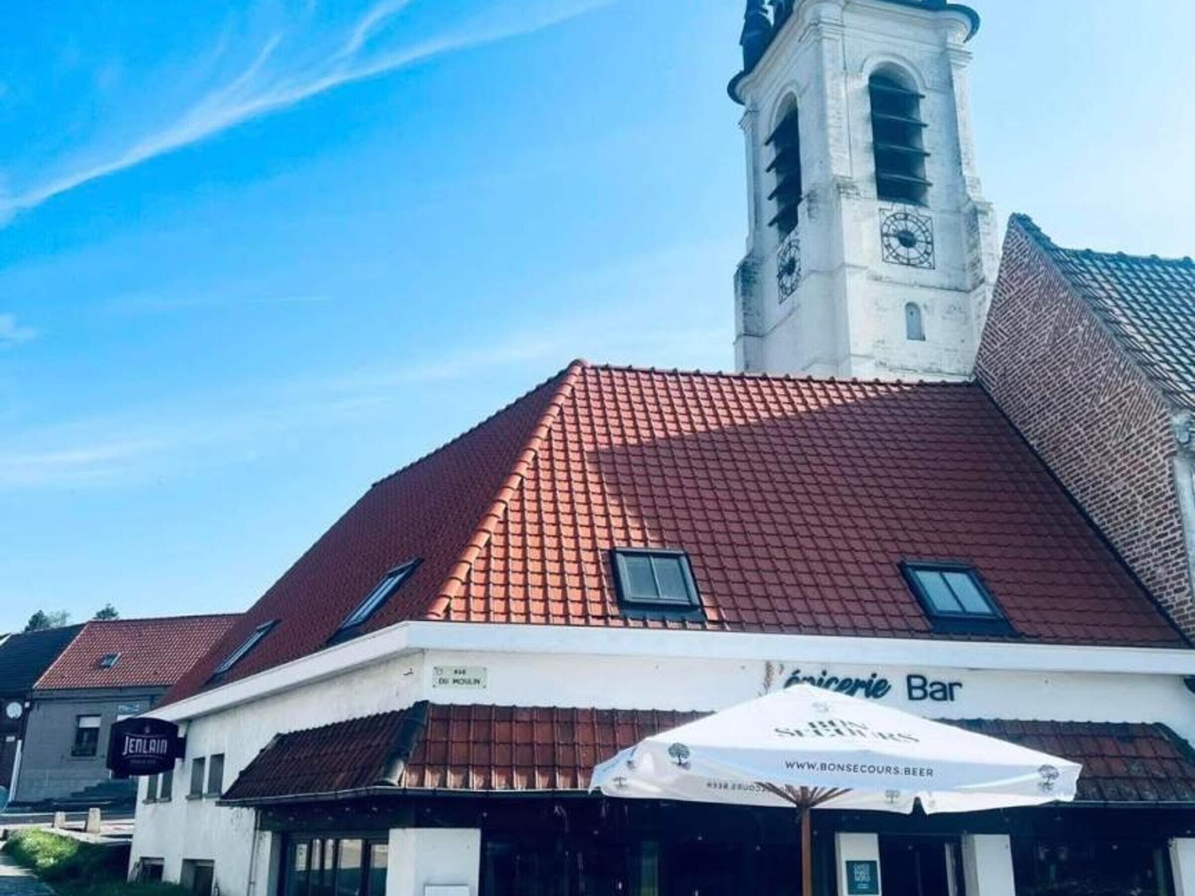 A building with a red-tiled roof, a clock tower, and a sign for 'JENLAIN Bar'.