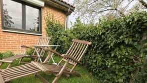 Un jardí amb una casa de maó, una banca de fusta i una taula.