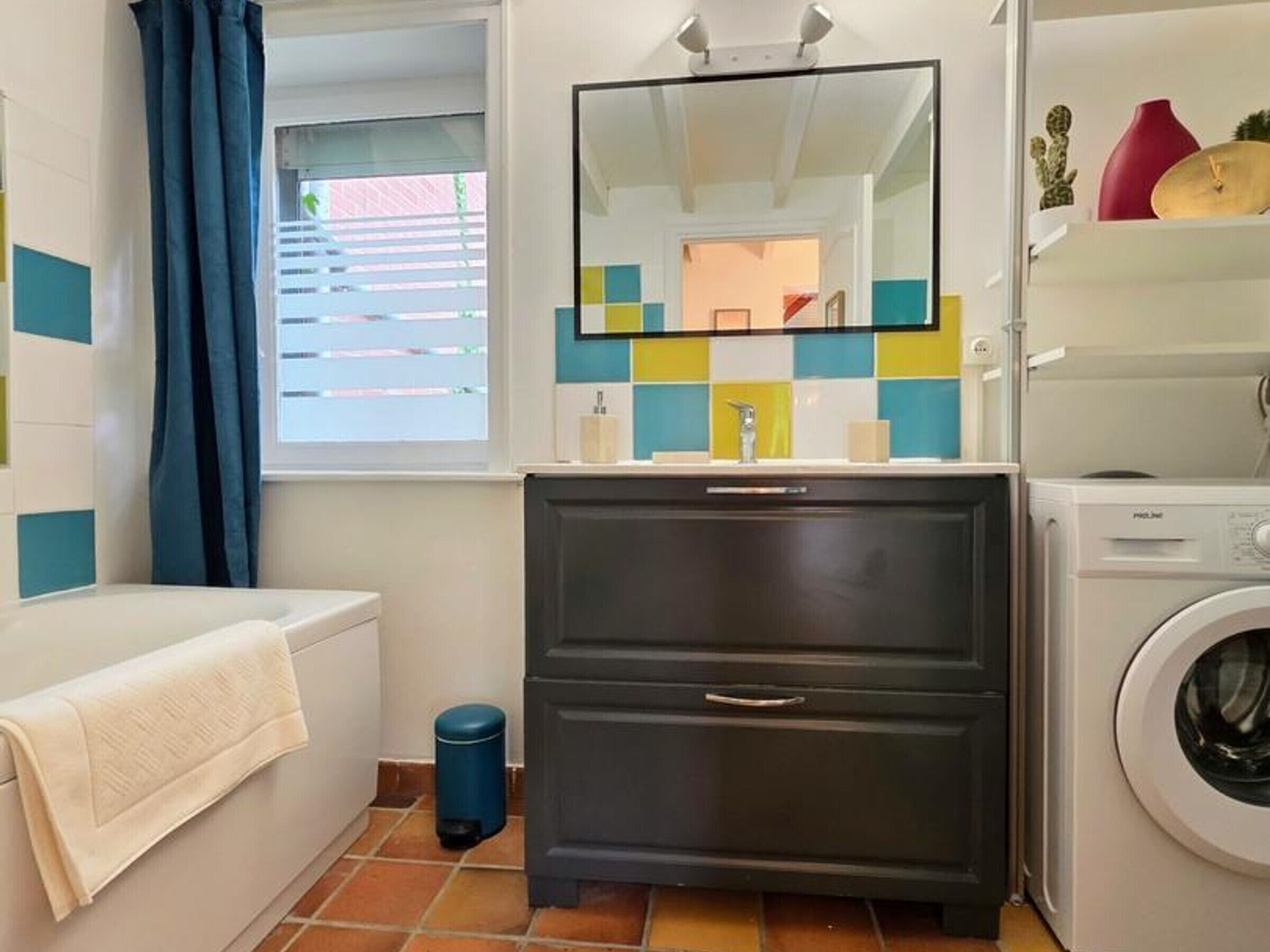 Une petite salle de bain comprenant des toilettes, un lavabo, un miroir, un lave-linge et une poubelle bleue.