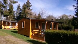 A wooden cabin with a porch, surrounded by greenery and trees. - Cozy mobile home with terrace - 4 guests (Dossenheim-sur-Zinsel)