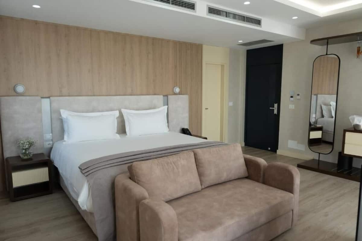 Una habitación de hotel moderna con una cama grande, un sofá, una mesita de noche, un espejo y una puerta.