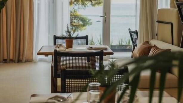 Une pièce comprenant une table à manger, des chaises, un canapé et donnant sur la mer.