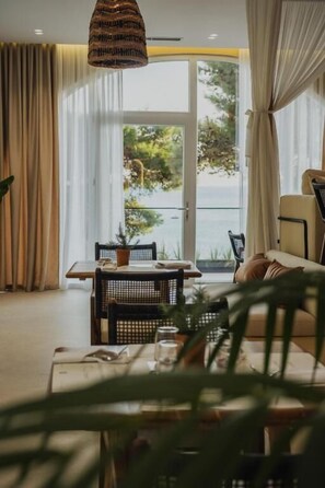 A room with a dining table, chairs, a sofa, and a view of the sea. - Great White Hotel (Shëngjin)