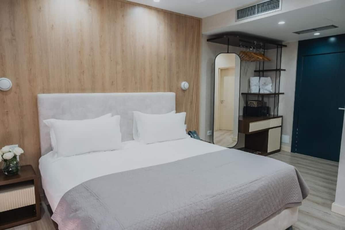 Una habitación de hotel moderna con una cama grande, una mesita de noche, un espejo y un armario.