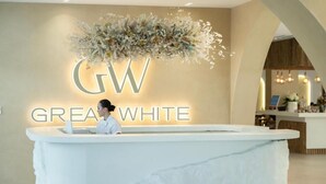 Un comptoir d’accueil surmonté d’un arrangement floral, et les mots « GW GREAT WHITE » illuminés sur le mur.