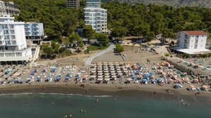 Une vue aérienne d’une plage avec de nombreux parasols et des chaises longues, entourée de bâtiments et d’arbres.