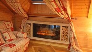 Interior acollidor d'una cabana amb una llar de foc, parets de fusta, un sofà amb coixins i cortines amb un disseny.