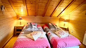 Un dormitori d'estil cabana amb dos llits, parets de fusta i un sostre inclinat.