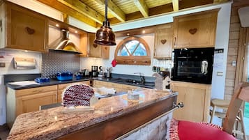 Eine Küche mit Holzausbau, einer Granit-Arbeitsplatte, einer hängenden Pendelleuchte und einem eingebauten Backofen.