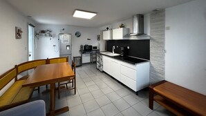 Cocina compacta con armarios blancos, encimera negra y estufa integrada. Hay una mesa de comedor con sillas y un banco.