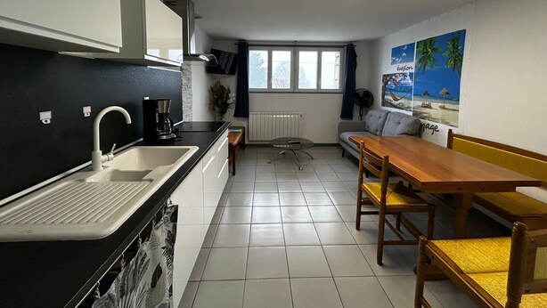 Cocina compacta con un lavamanos, una cafetera y un ventanal. Zona de comedor con una mesa y sillas.