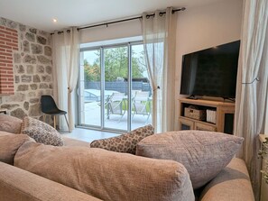 A living room with a stone wall, a sofa with patterned cushions, a TV, and a sliding glass door leading to an outdoor patio. - House with pool, pets allowed - 6 guests (Saint-Victor-Malescours)