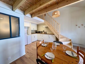 Eine moderne Küche mit weißen Schränken, einer Holztreppe und einem Essbereich mit rundem Tisch, gedeckt für vier Personen.
