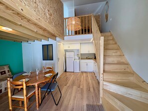Ein Essbereich mit Holztisch und -stühlen, eine Küche mit weißen Schränken und eine Holztreppe.