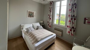 Une chambre à coucher comprenant un lit, une table de chevet, une chaise, une fenêtre avec des rideaux, un radiateur et un ventilateur de plafond.