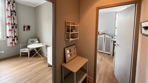 Une pièce avec un plancher en bois, une chaise blanche, une petite table, un miroir et une étagère ornée d’objets décoratifs.