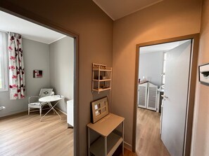 Ein Zimmer mit Holzboden, einem weißen Stuhl, einem kleinen Tisch, einem Spiegel und einem Regal mit Dekoration.