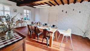 A dining area with a wooden table set for four, surrounded by chairs, a vase with flowers, and a window with blinds. - Independent house, pets welcome - 6 guests (VENDEGIES SUR ECAILLON)
