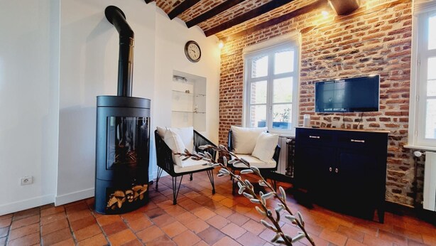 A living room with a brick wall, a fireplace, a television, and a sofa. - Independent house, pets welcome - 6 guests (VENDEGIES SUR ECAILLON)