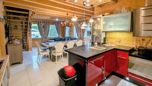 Una cocina moderna con armarios rojos, encimera negra y electrodomésticos de acero inoxidable. Hay un comedor con sillas blancas y una banca.