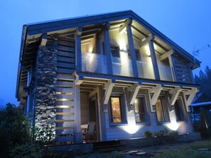 En toetage-hytte med en facade af sten, store vinduer og en veranda med udendørs møbler.