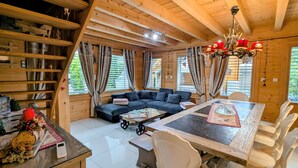 Una cabaña de madera acogedora con una mesa de comedor, sillas blancas, un sofá y una araña.