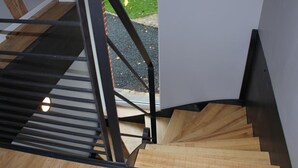 A wooden staircase with metal railings, leading to a landing with a glass door.