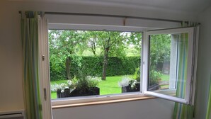 A dining area with a table set for two, a window with a view of a garden, and a chair.