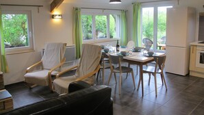 A dining area with a table set for four, surrounded by chairs, a sofa, and a kitchen area with a refrigerator and oven.