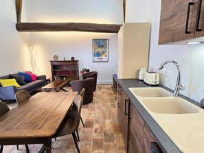 A modern kitchen with a wooden table, a sofa, and a bookshelf.
